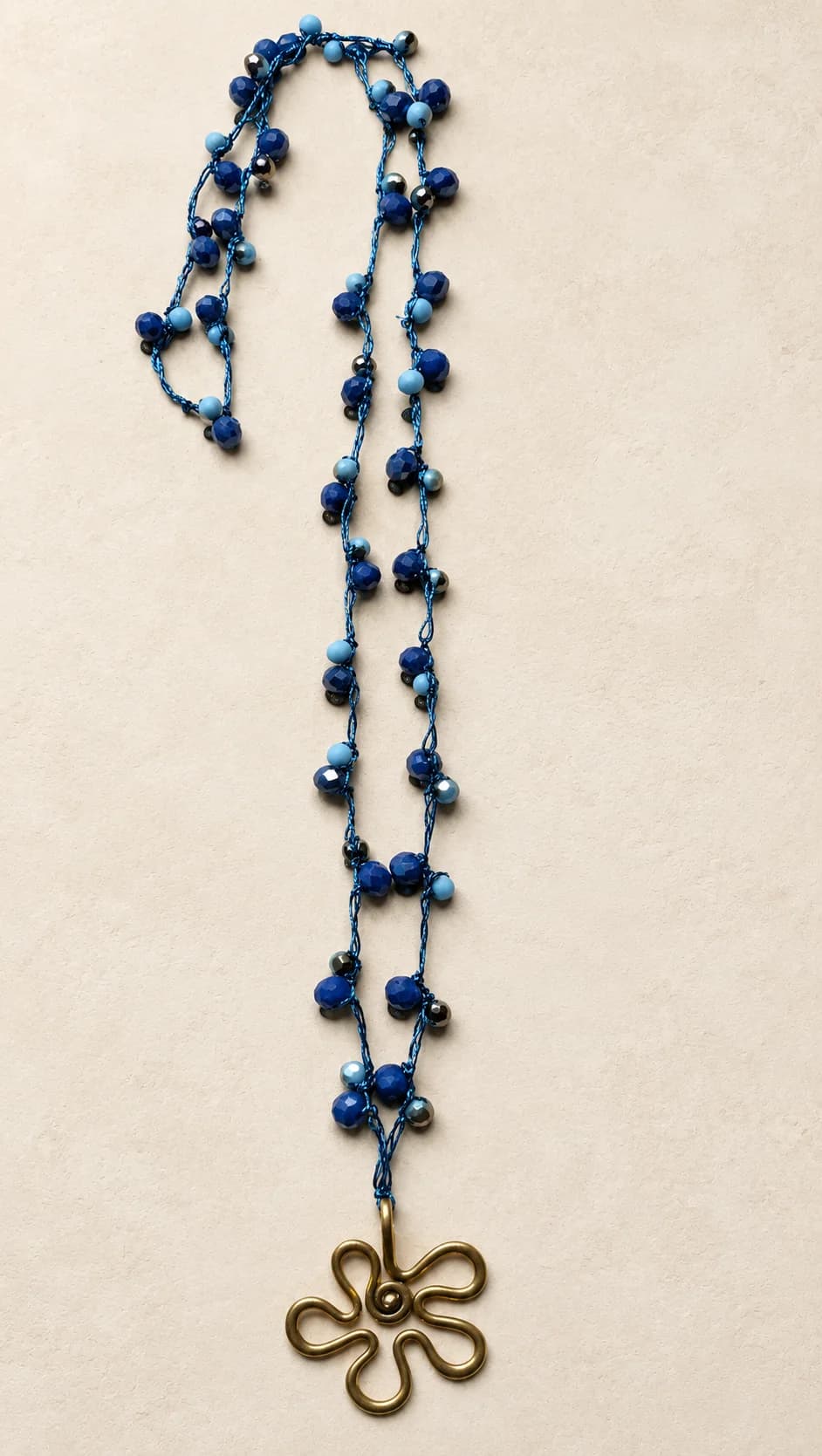 Elementi blu di forme diverse lungo un filo annodato e pendente aperto a forma di fiore.