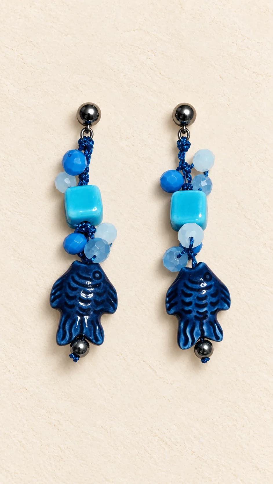 Coppia di orecchini con elementi tondi e squadrati blu e turchesi, piccoli dettagli chiari e pendenti a pesce blu.