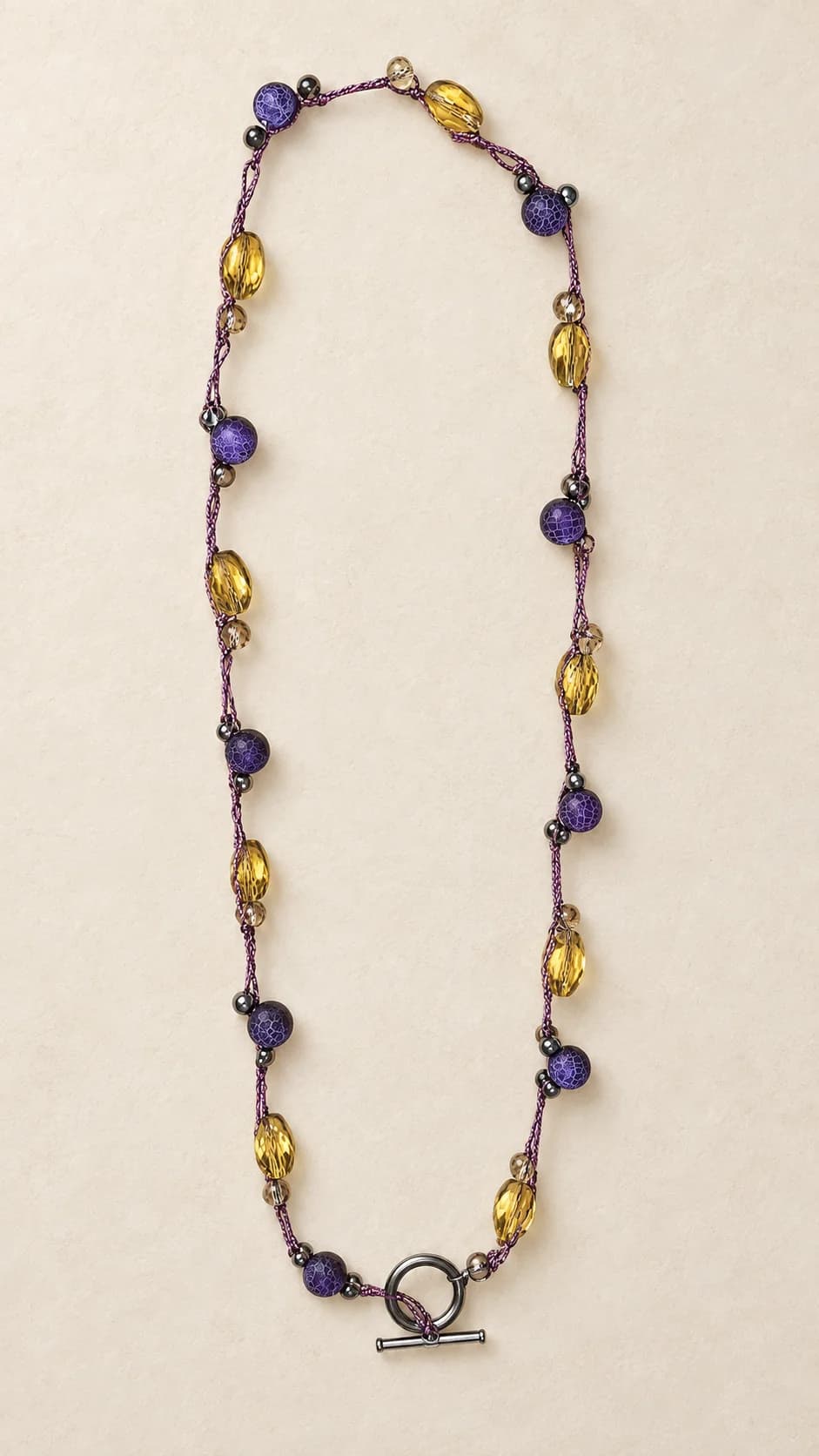 Elementi viola e giallo dorato intervallati lungo il filo, con chiusura a barretta. La scheda riguarda la sola collana: gli orecchini nella foto non sono inclusi. Il nome descrive i colori.