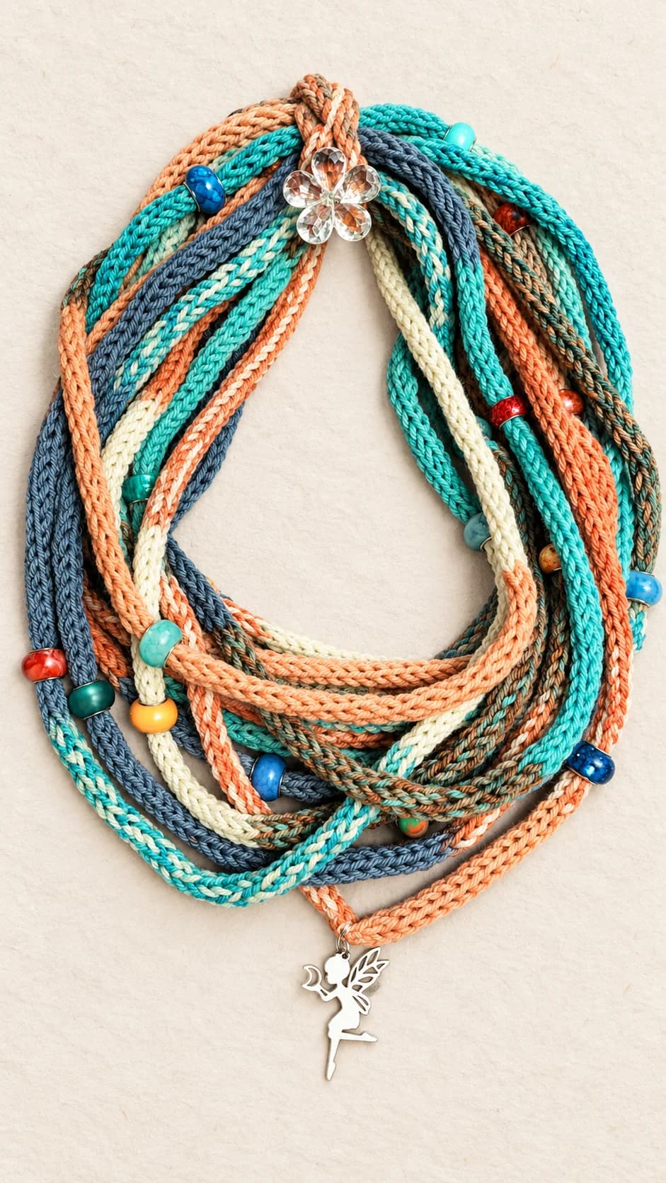 Collana a più fili in lana merinos lavorata, con sfumature turchesi, corallo, crema e grigio, perle decorative, fiore trasparente e charm a forma di fata.