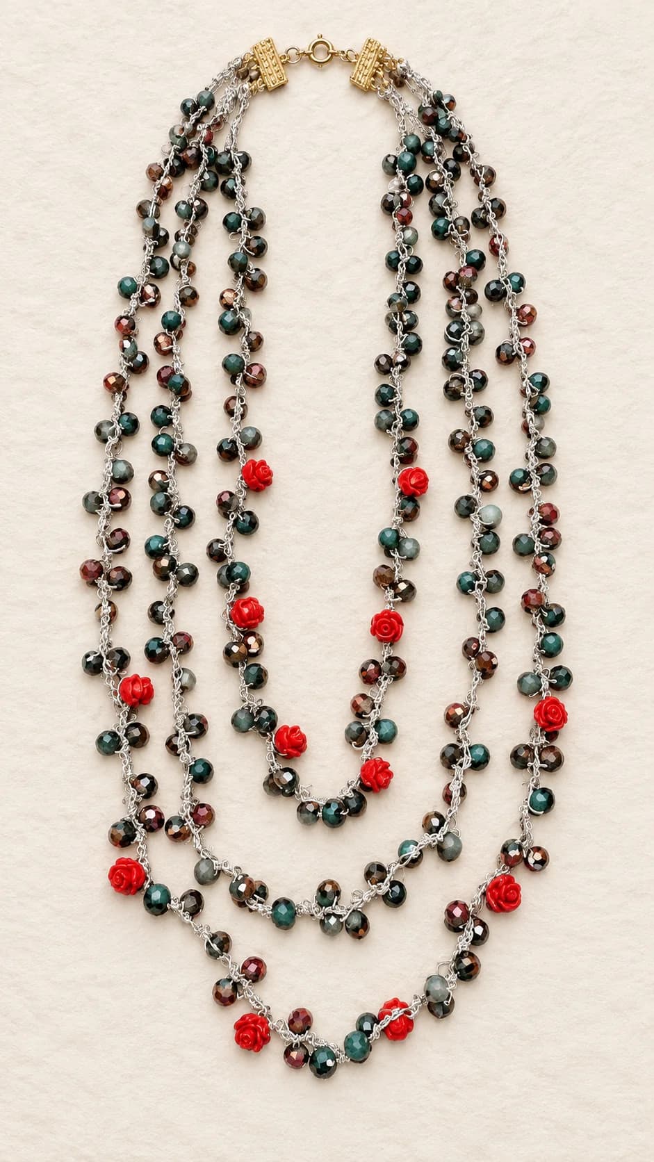 Collana a tre fili di diversa lunghezza, con elementi sfaccettati verde scuro e bronzo, piccole rose rosse e chiusura dal tono dorato.
