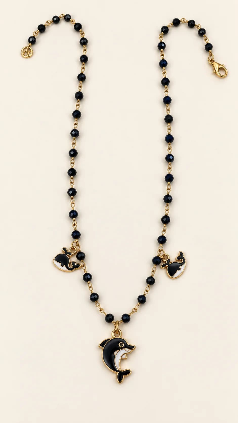 Collana con perline nere sfaccettate collegate da maglie dorate, due balene nere e bianche laterali e un delfino centrale coordinato.