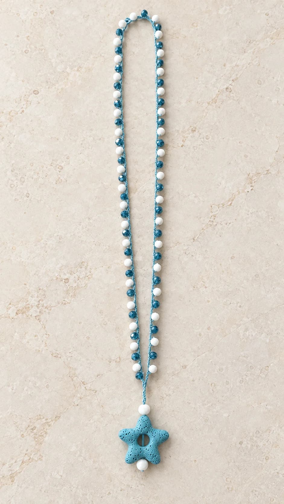 Collana nei toni azzurro e bianco, con piccoli elementi sfaccettati e pendente centrale a forma di stella marina.
