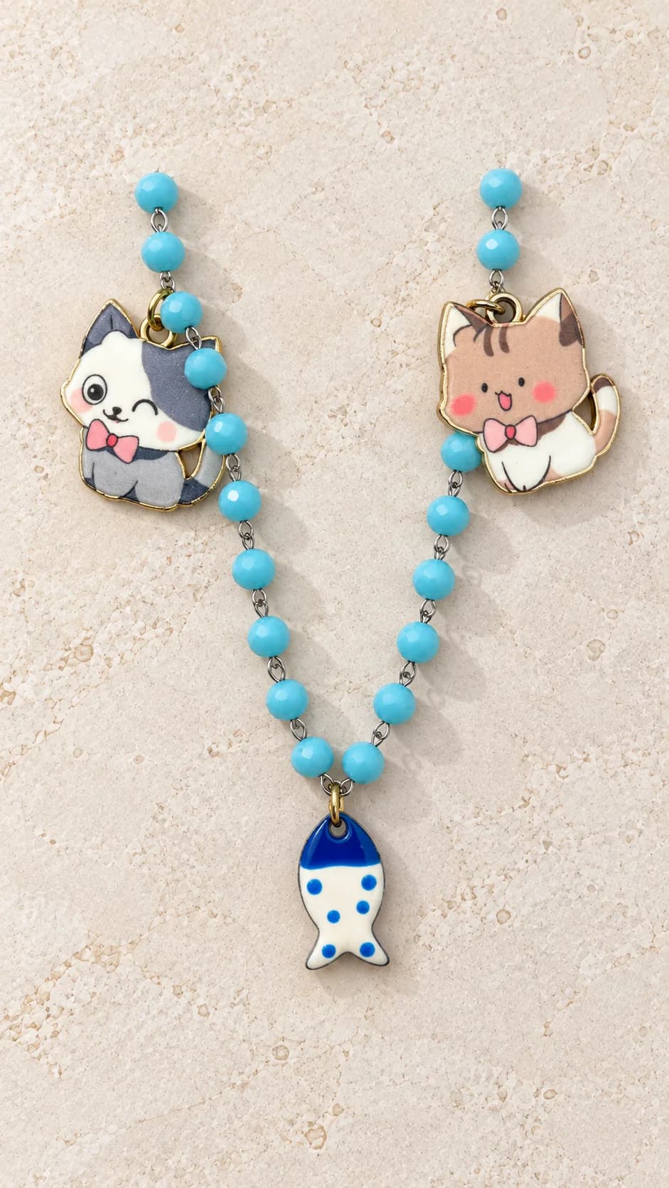Collana con elementi turchesi sfaccettati, due pendenti a forma di gatto e pesce centrale bianco e blu.