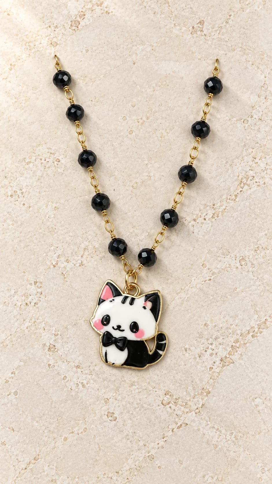 Collana con elementi neri sfaccettati, collegamenti dal tono dorato e pendente a forma di gattino bianco e nero.