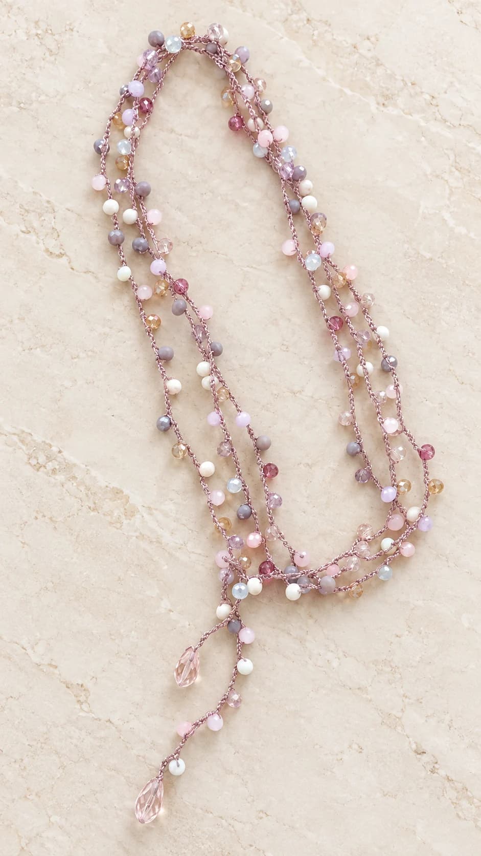 Collana a più fili nei toni rosa, lilla, cipria e bianco, con piccoli elementi sfaccettati e chiusura frontale a cravatta.