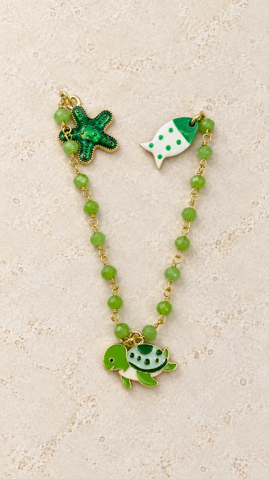 Collana con elementi verdi sfaccettati, tartaruga centrale e dettagli laterali a stella marina e pesce.