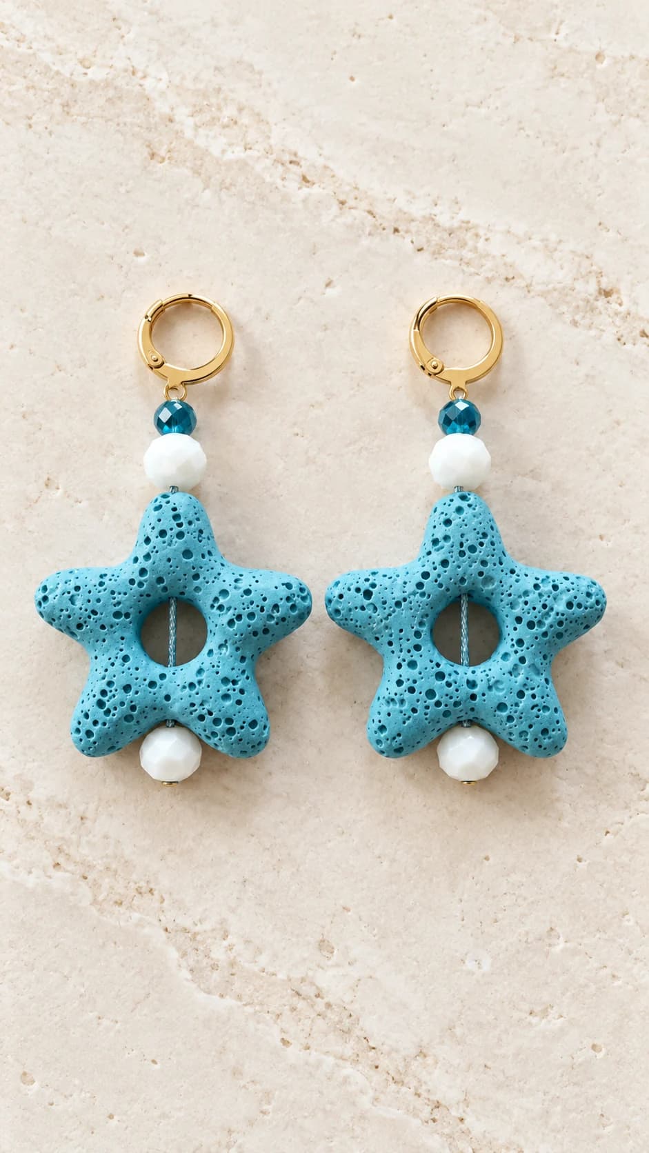Coppia di orecchini pendenti con stelle marine azzurre, elementi sfaccettati bianchi e blu e attacchi dal tono dorato.
