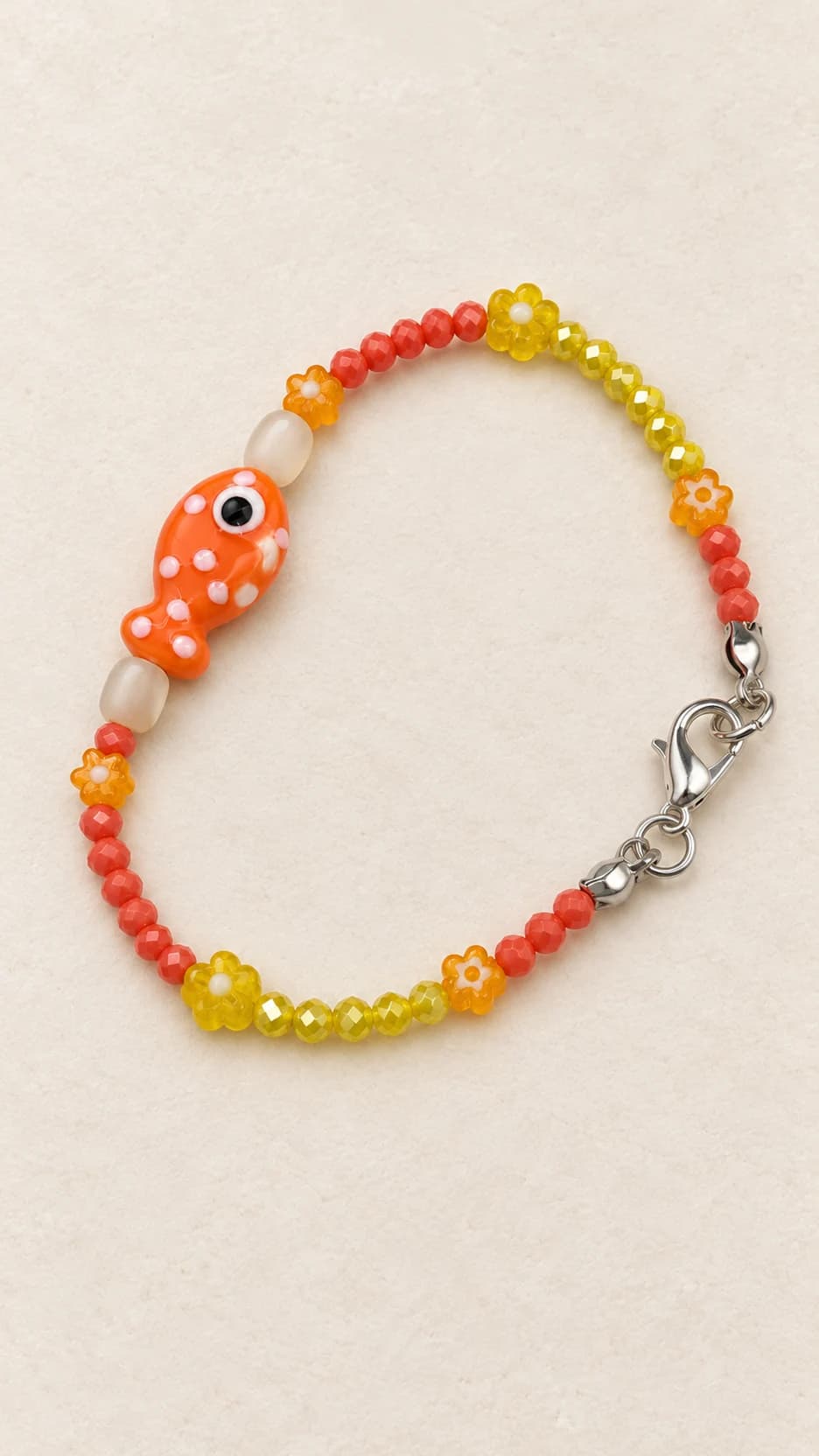 Bracciale con pesce arancio, due elementi ovali color avorio ai suoi lati, perline arancio e gialle e chiusura dal tono argentato. Non ha nappe.