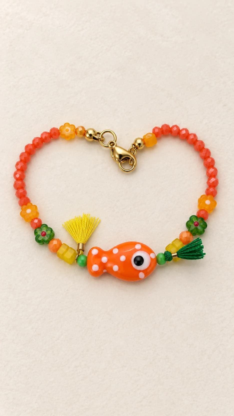 Bracciale con pesce arancio, perline corallo, fiori arancio e verdi, due nappe gialla e verde e chiusura dal tono dorato.