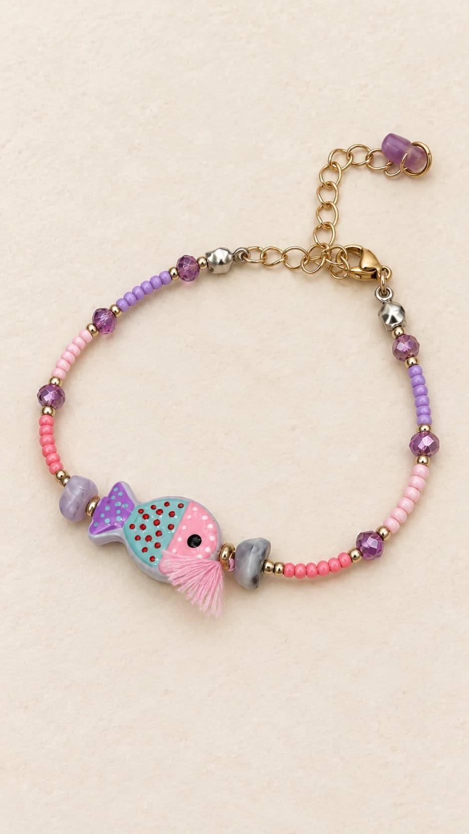 Bracciale con pesce rosa e verde acqua, perline rosa e viola, elementi decorativi coordinati e chiusura con catenella dal tono dorato.