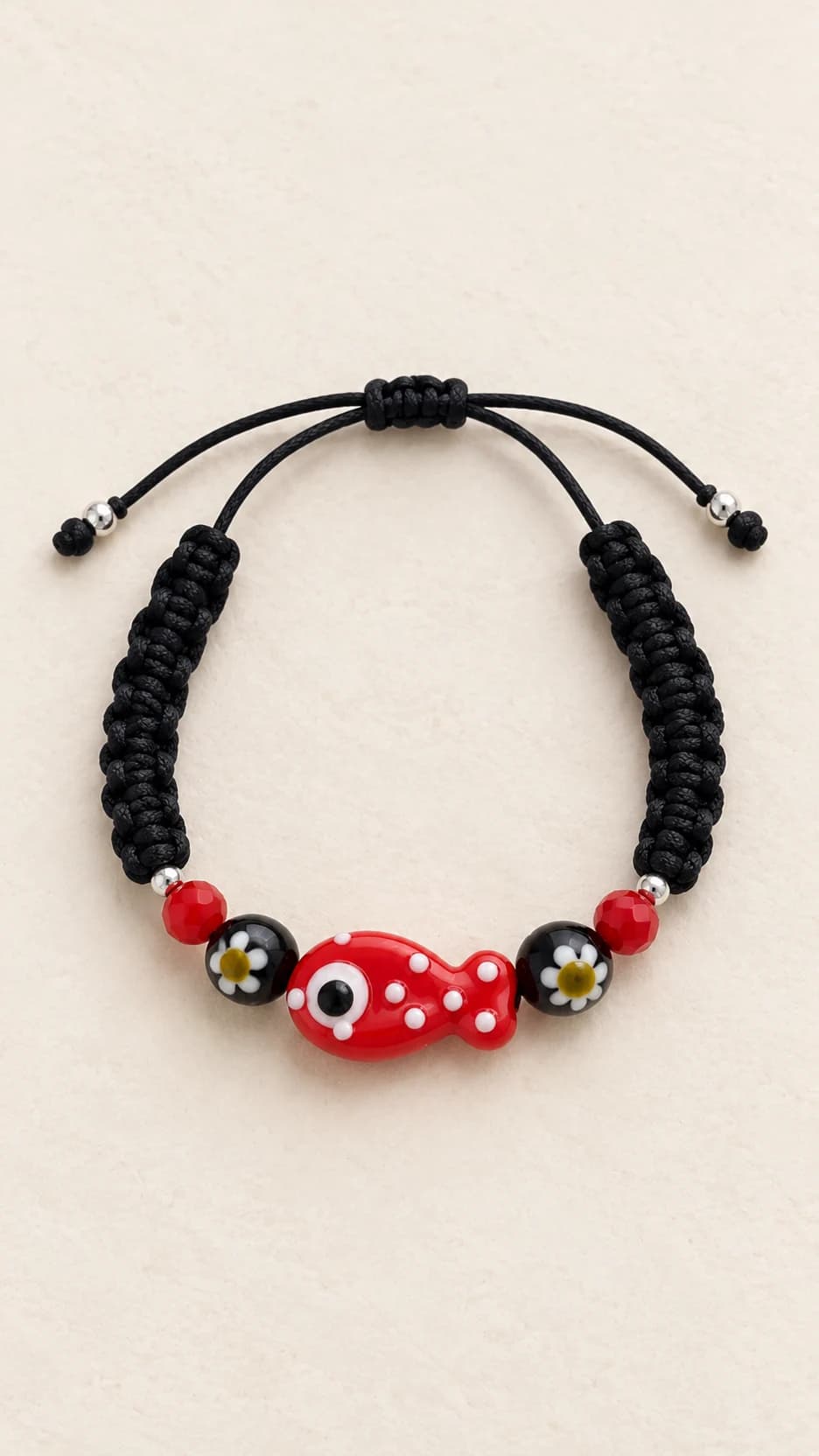 Bracciale con cordino nero intrecciato, pesce rosso a pois bianchi, piccoli elementi rossi e decorazioni scure. Chiusura a cordino.