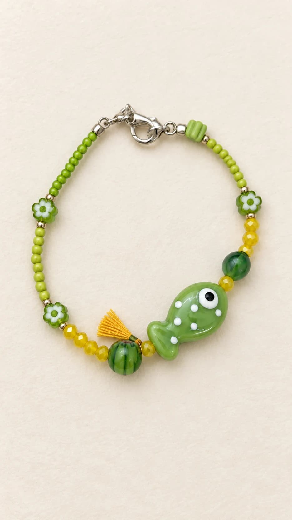 Bracciale con pesce verde a pois, elementi verdi e gialli, piccola nappina gialla e chiusura dal tono argentato.
