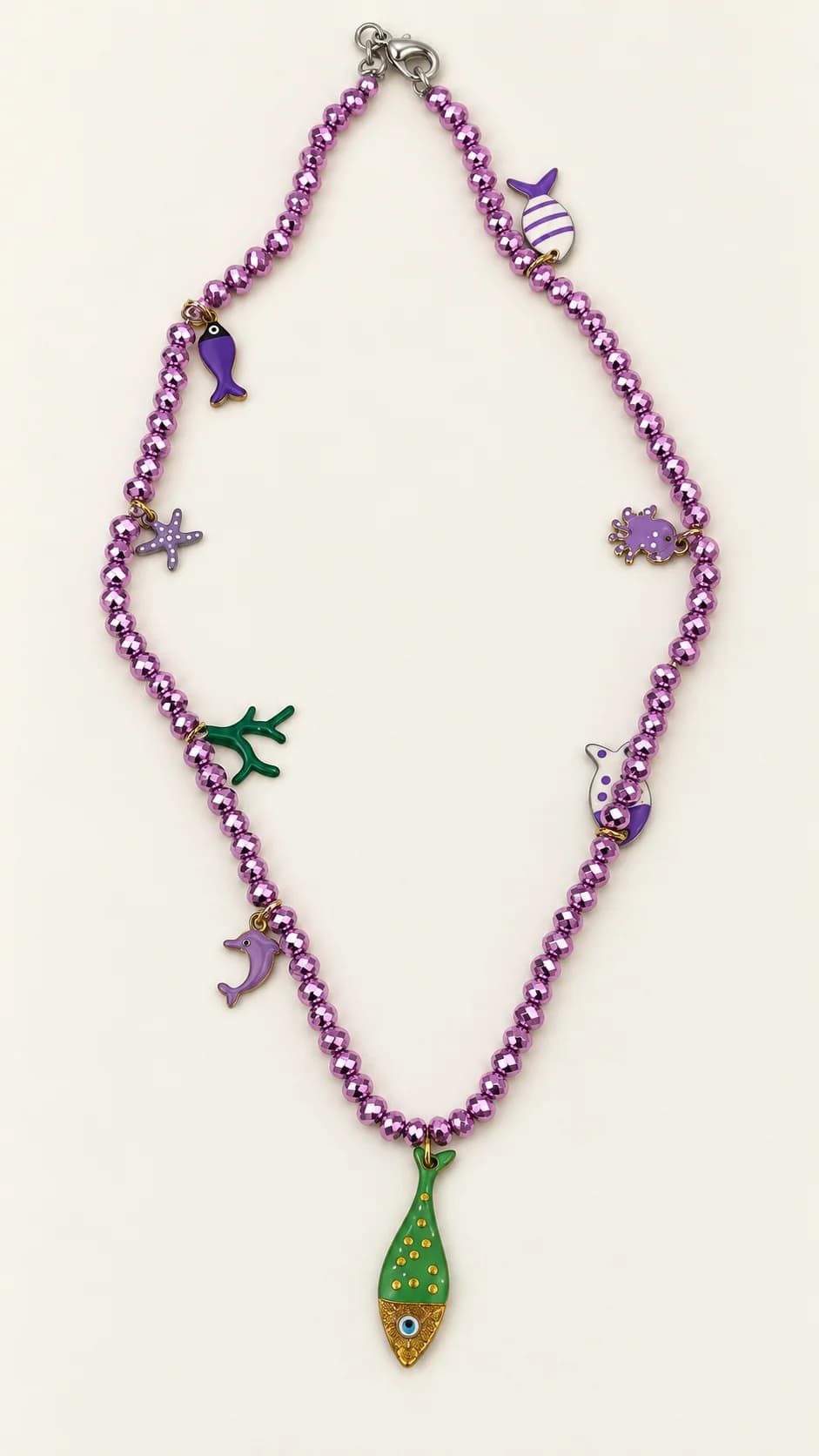 Collana di perline viola sfaccettate con otto pendenti: due piccoli pesci, stella marina, granchio, corallo verde, balena, delfino e un pesce verde e oro centrale.